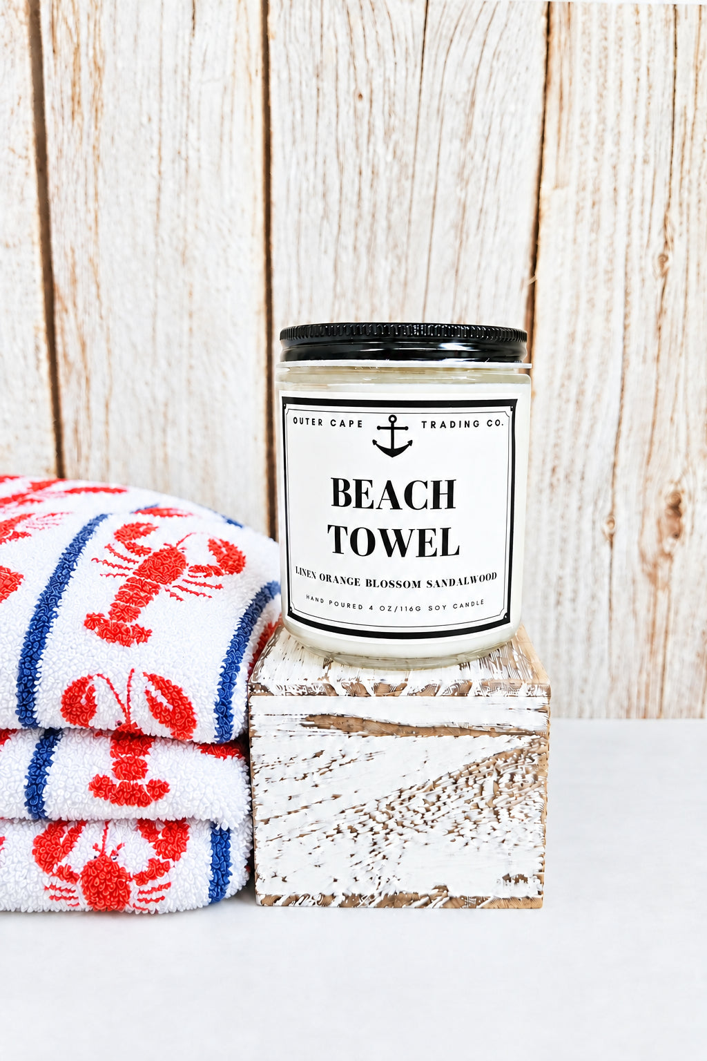 Candle labeled 'Beach Towel' on a wooden block with a wooden background