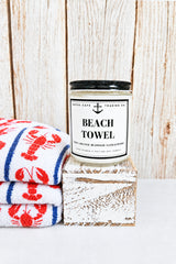Candle labeled 'Beach Towel' on a wooden block with a wooden background