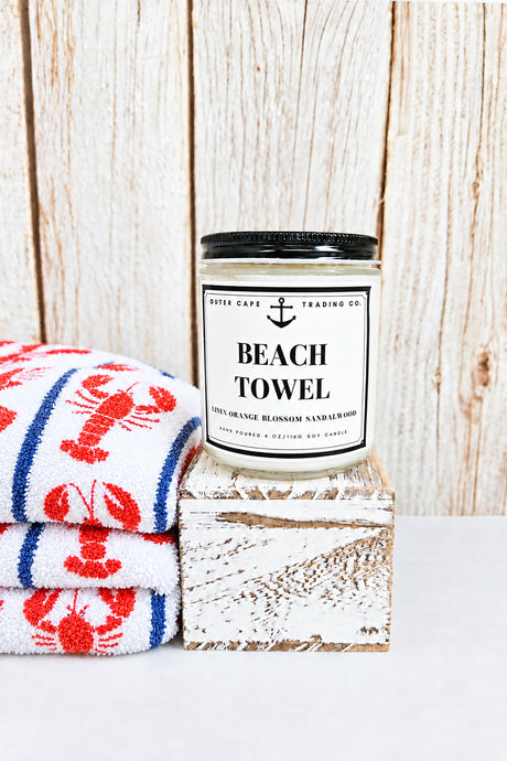 Candle labeled 'Beach Towel' on a wooden block with a wooden background