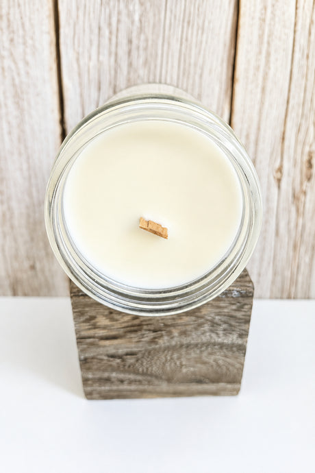 Candle in a glass jar with a wooden base on a white surface with a wooden background