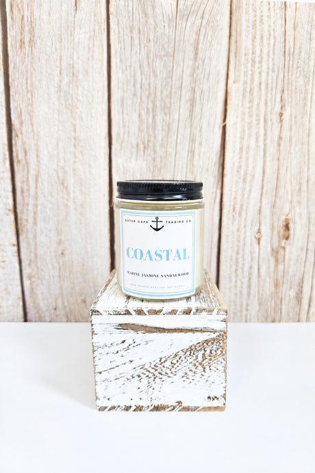 Candle labeled 'Coastal' on a wooden block with a wooden background