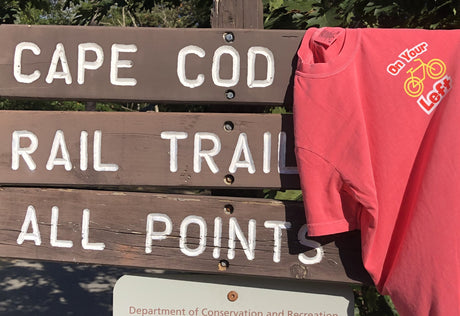 Cape Cod Rail Trail donation t-shirt hanging on a rustic wooden park sign to support trail projects.