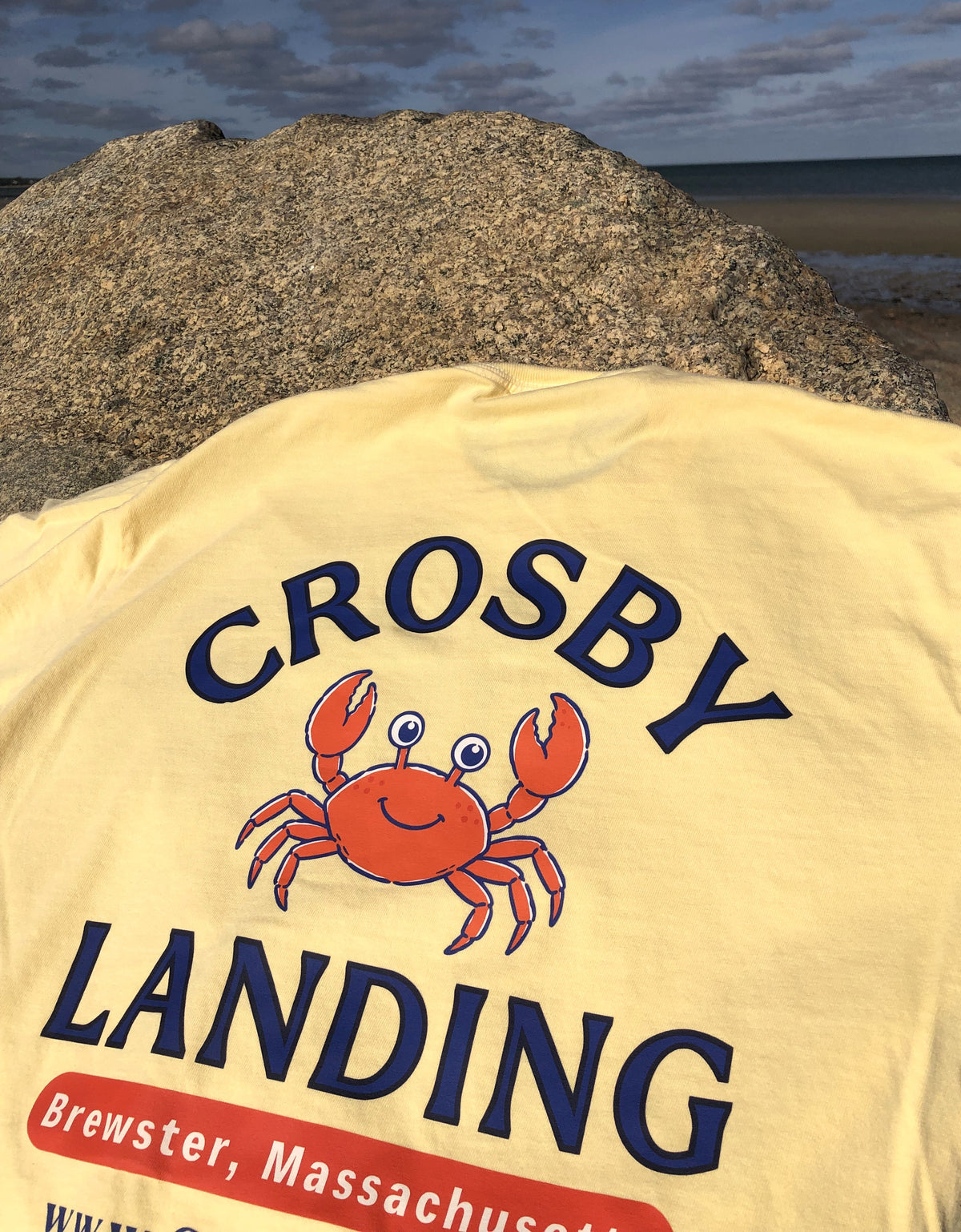 Crosby Beach Cape Cod t-shirt in butter displayed on a weathered rock at the ocean jetty.