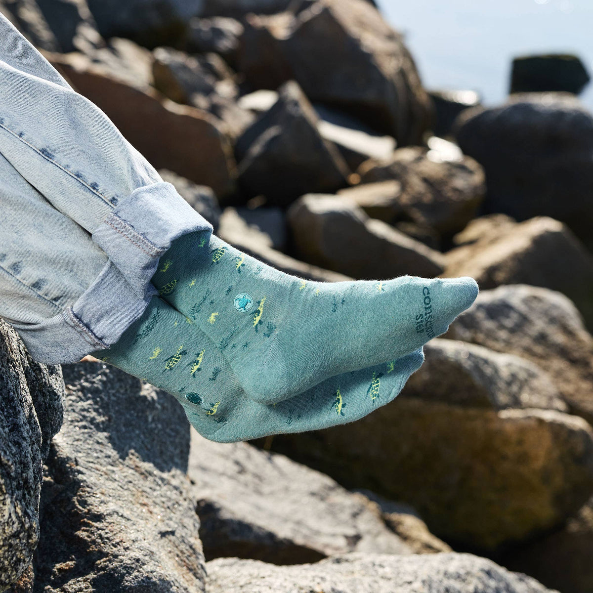 Close-up of a person with crossed legs wearing organic cotton sea turtle protection socks to showcase the knit graphic design.