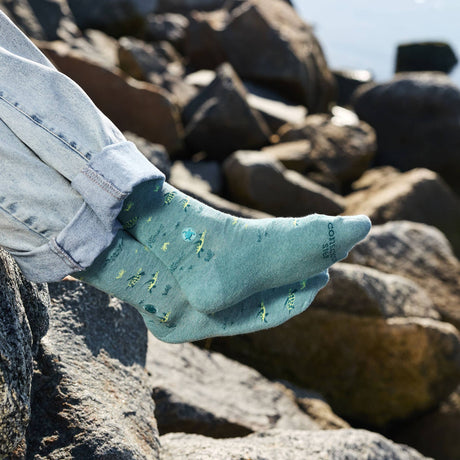 Close-up of a person with crossed legs wearing organic cotton sea turtle protection socks to showcase the knit graphic design.
