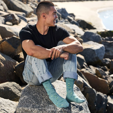 A man wearing organic cotton sea turtle protection socks while sitting on a coastal rock.