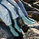 People sitting on coastal rocks wearing organic cotton socks that support sea turtle conservation, showing a casual lifestyle view of the eco-friendly apparel.